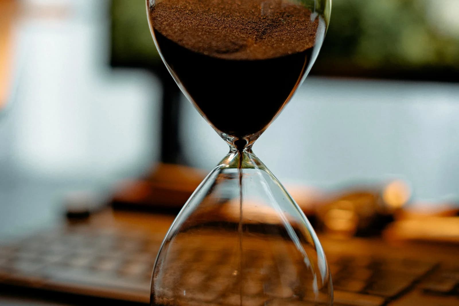 Hourglass with dark sand on a desk in front of a monitor